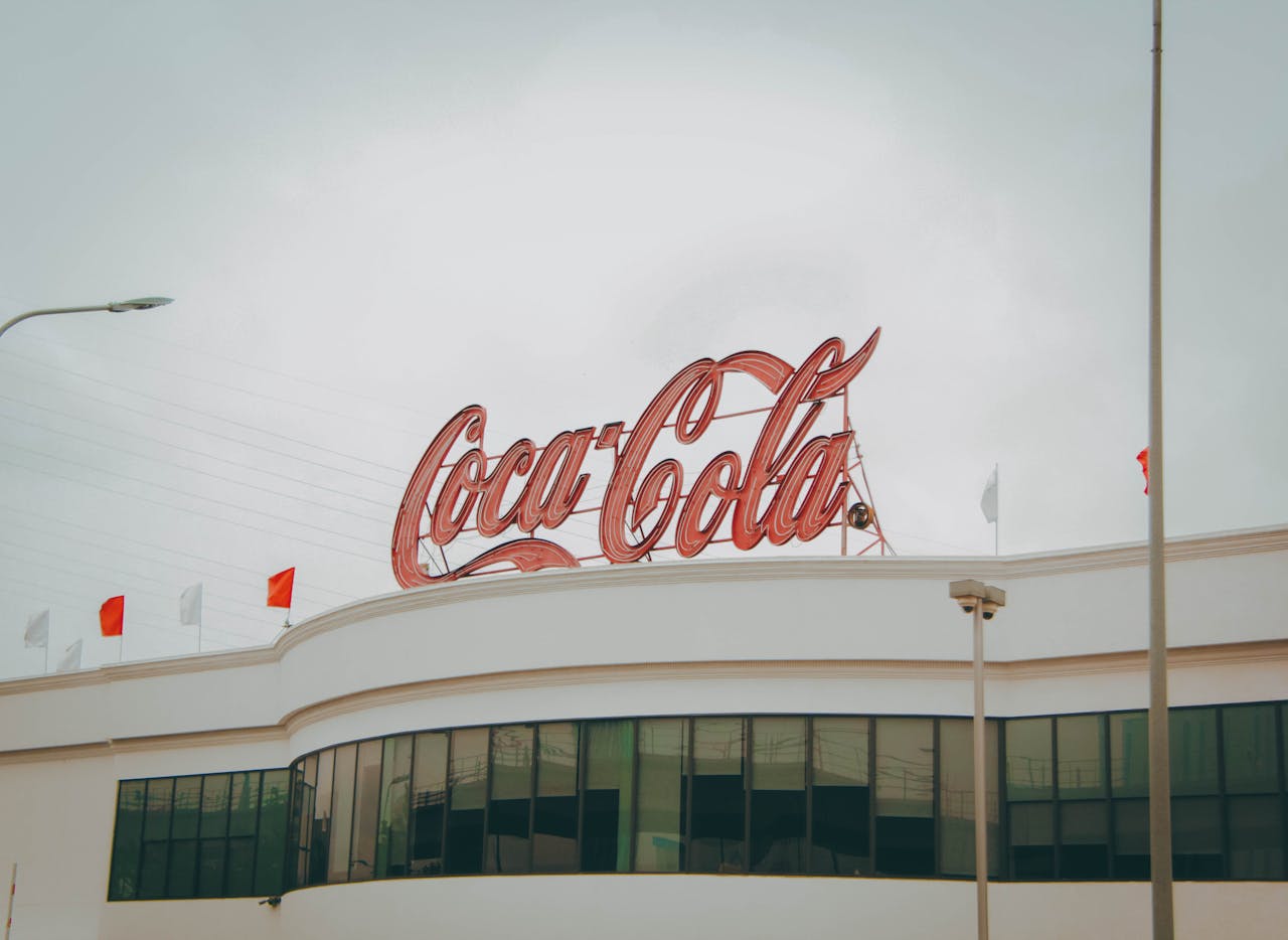 services-01 Exterior view of Coca-Cola factory with iconic red sign atop the modern building.